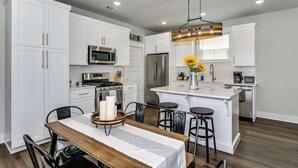 A modern kitchen with white cabinetry, stainless steel appliances, a central island with bar stools, and a hanging light fixture.