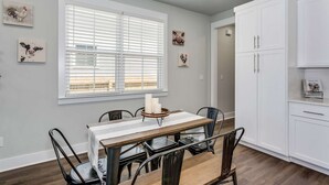 A dining area with a table and chairs, a window with blinds, and white cabinets.