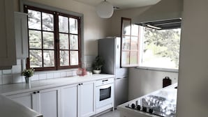 Une cuisine avec des meubles blancs, une cuisinière, un évier et une fenêtre donnant sur des arbres.