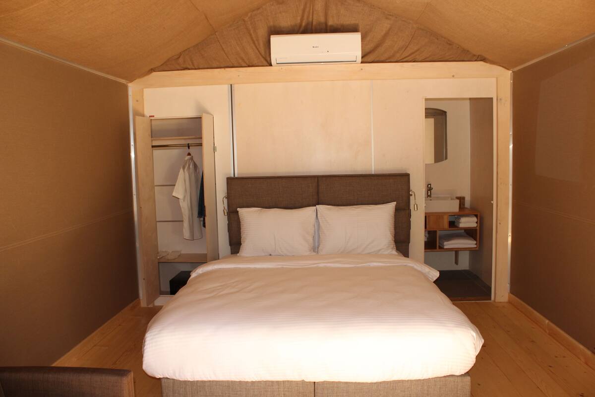 A bedroom with a large bed, a wardrobe, a mirror, and a small bedside table.