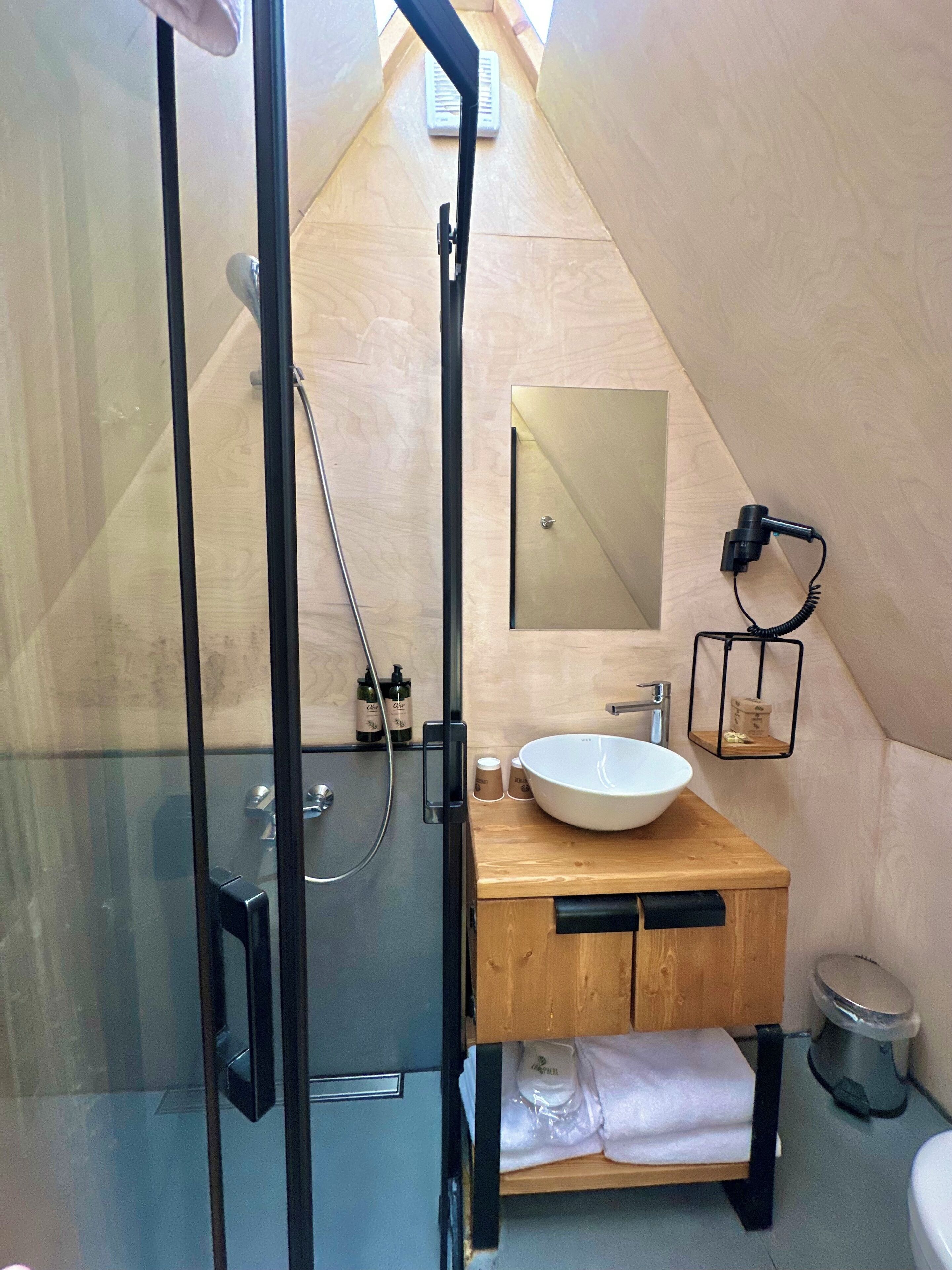 Ein modernes Badezimmer mit einer Duschkabine aus Glas, einem Holzwaschtisch mit weißem Waschbecken und einem kleinen Spiegel.