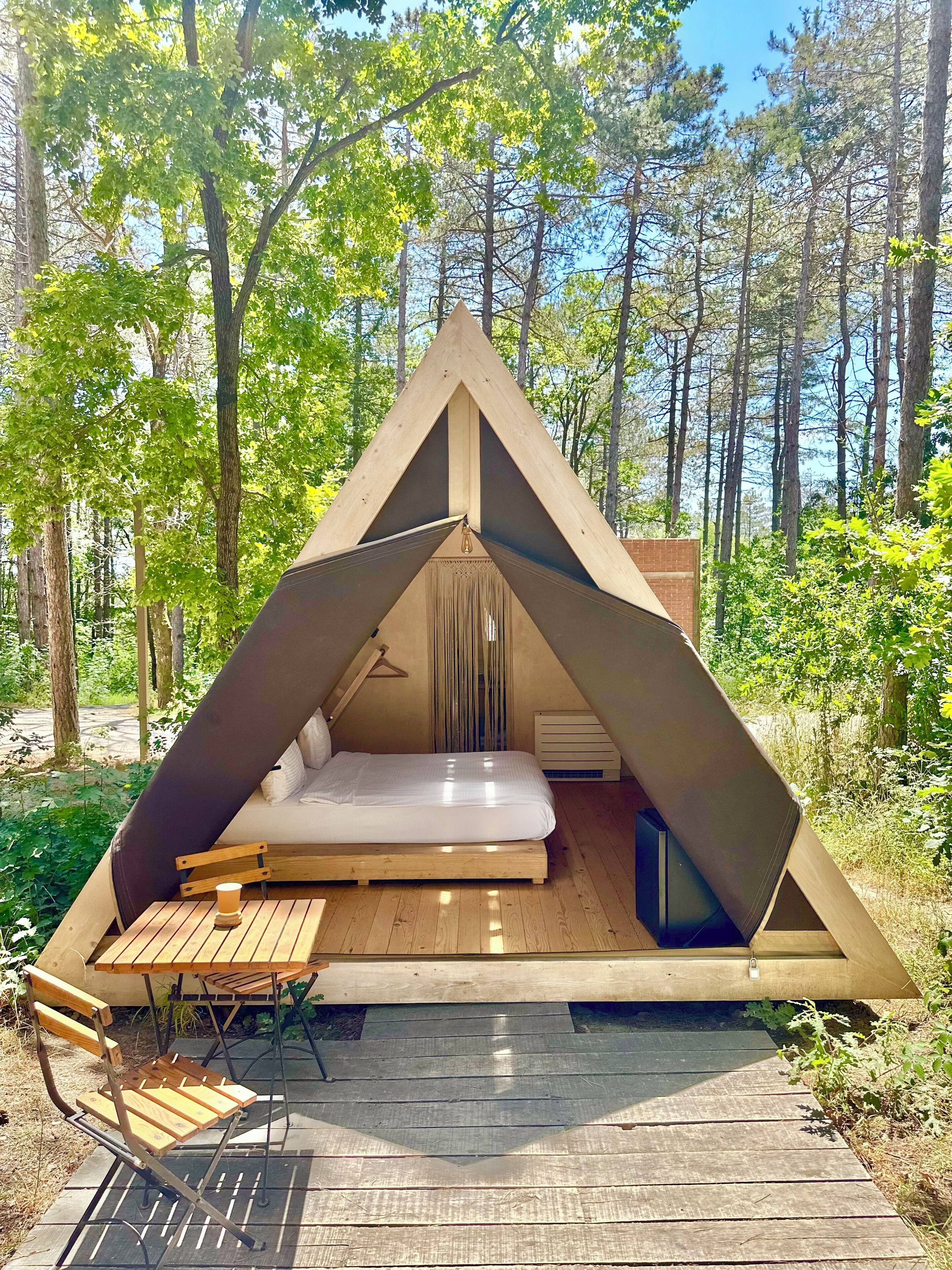 Una estructura tipo tienda triangular con una cama, una mesa y una silla.