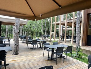 An outdoor patio area with tables and chairs, surrounded by trees and wooden structures. - Longosphere Glamping (Demirköy)