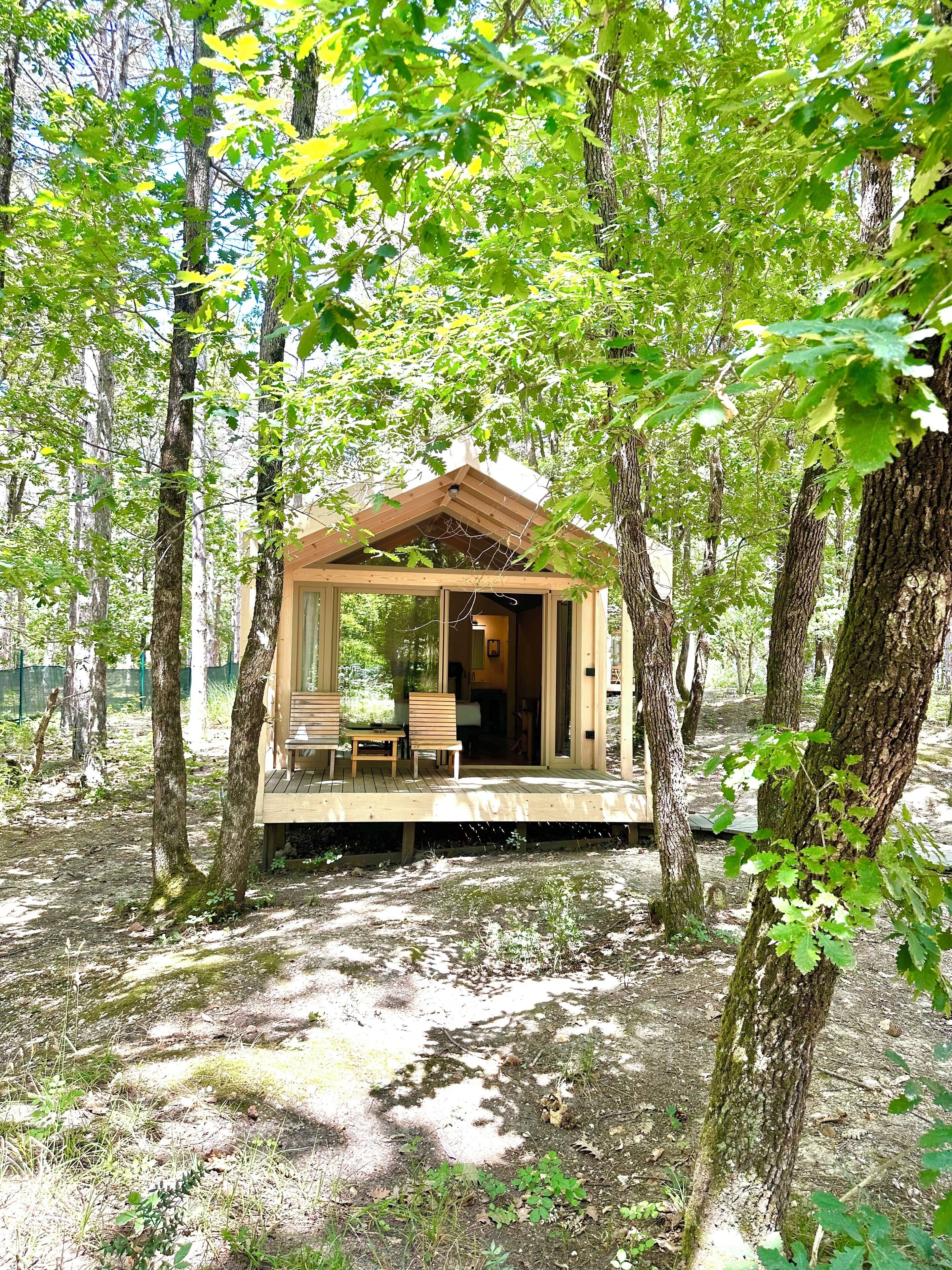 A wooden cabin with a deck, surrounded by trees.