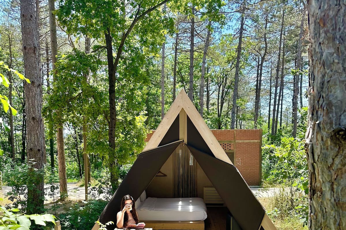 A wooden tent with a bed inside, surrounded by a forest.