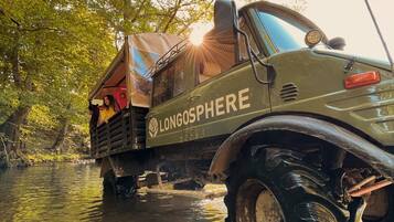 Un véhicule sur lequel on peut lire le mot « LONGOSPHERE » sur le côté, partiellement immergé dans une rivière bordée d’arbres.