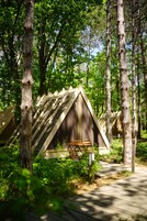 Un área boscosa con cabañas de madera triangulares, una mesa de picnic y un camino pavimentado.