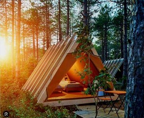 A triangular wooden structure in a forest with a bed inside. - Longosphere Glamping (Demirköy)