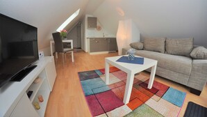 Un espace de vie compact comprenant un téléviseur, un canapé, une table basse et un tapis coloré.