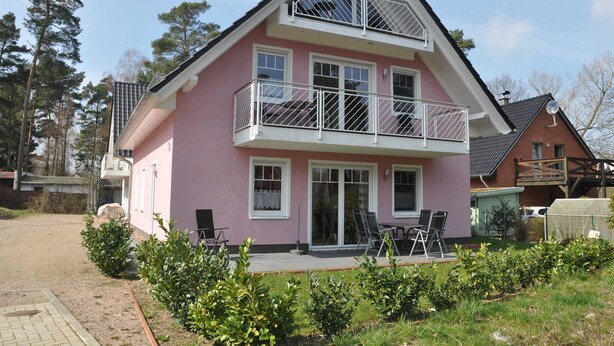 Une maison à deux étages dotée d’un balcon, d’une terrasse couverte et d’un jardin.