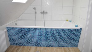 Une salle de bain avec une baignoire sur pieds, des murs carrelés et une lucarne.