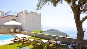 A poolside area with lounge chairs, a stone wall, and a view of the sea. - Apartment Giove With Sea View & Pool (Nerano)