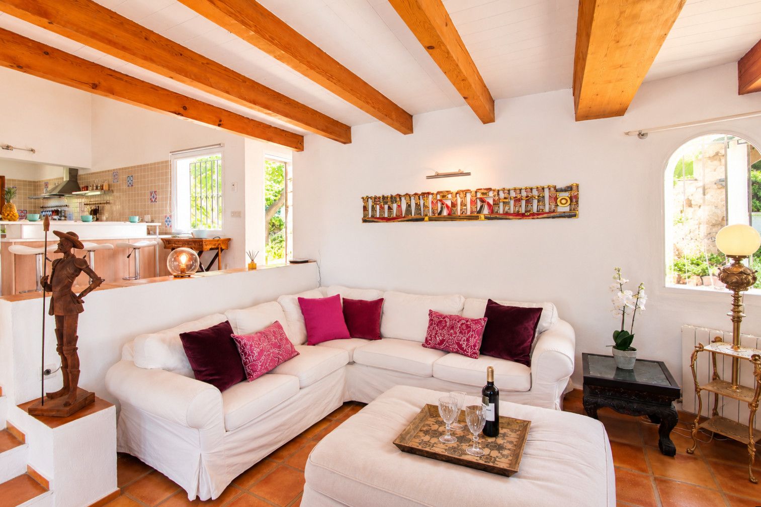A spacious living area with a white sectional sofa, a wooden sculpture, and a tray with glasses and a bottle.