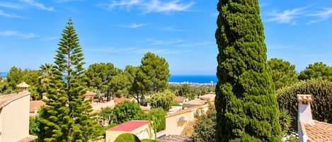 Un pueblo costero con arquitectura mediterránea, que incluye tejados de teja y paredes de estuco, rodeado de vegetación exuberante y cipreses.