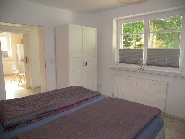 Un dormitorio con cama, ventana con persianas, radiador y armario.