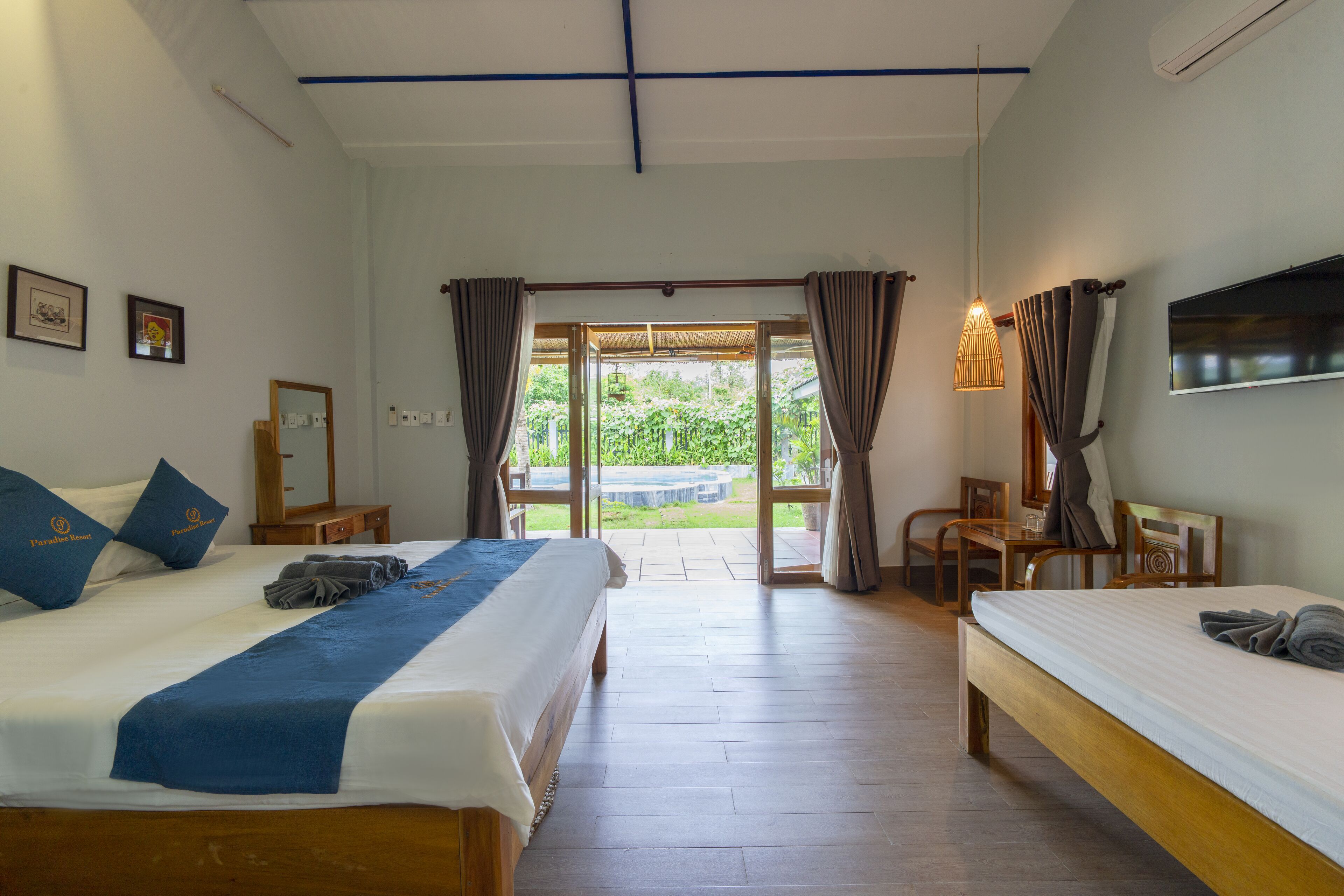 A hotel room with two beds, a desk, and a view of the garden.