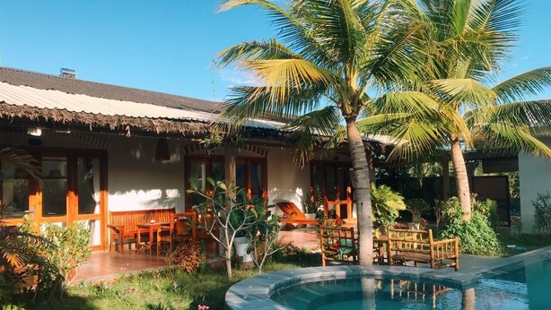 A poolside area with a thatched-roof building, wooden furniture, and a palm tree. - Green Bungalow Phu Quoc (Phu Quoc)