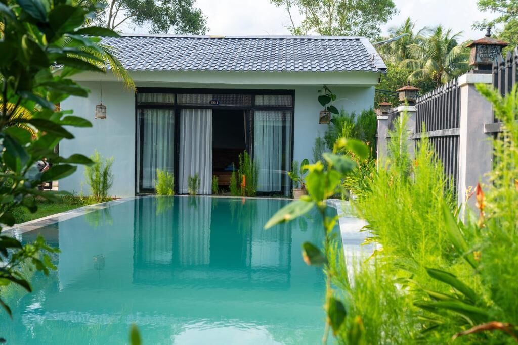 Uma casa moderna com piscina, cercada por vegetação exuberante e um portão fechado.