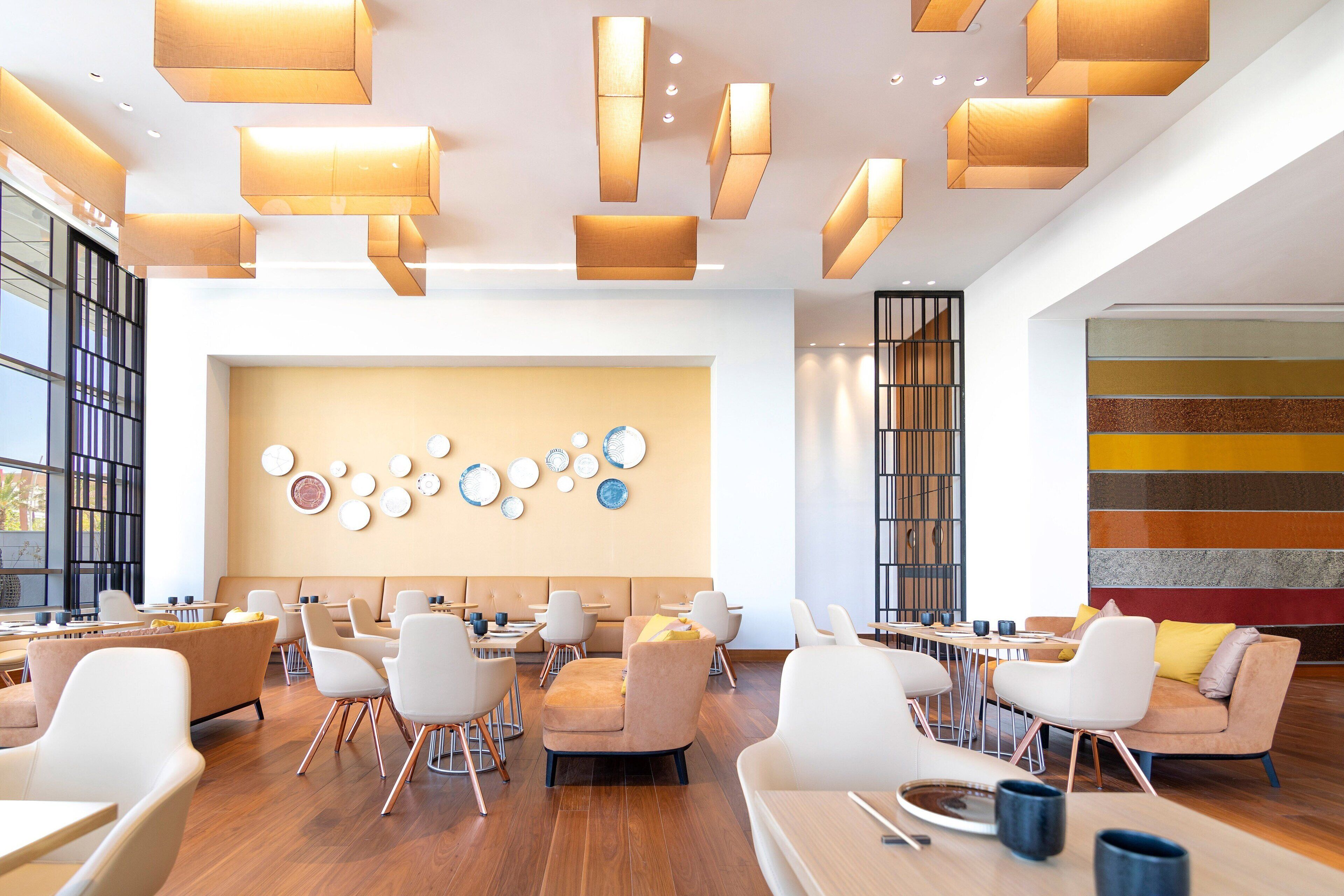 A modern dining area with multiple tables and chairs, a wall with circular plates, and a striped wall on the right.