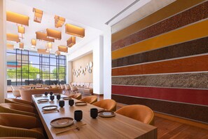 A modern dining area with a long wooden table set for a meal, surrounded by comfortable chairs.