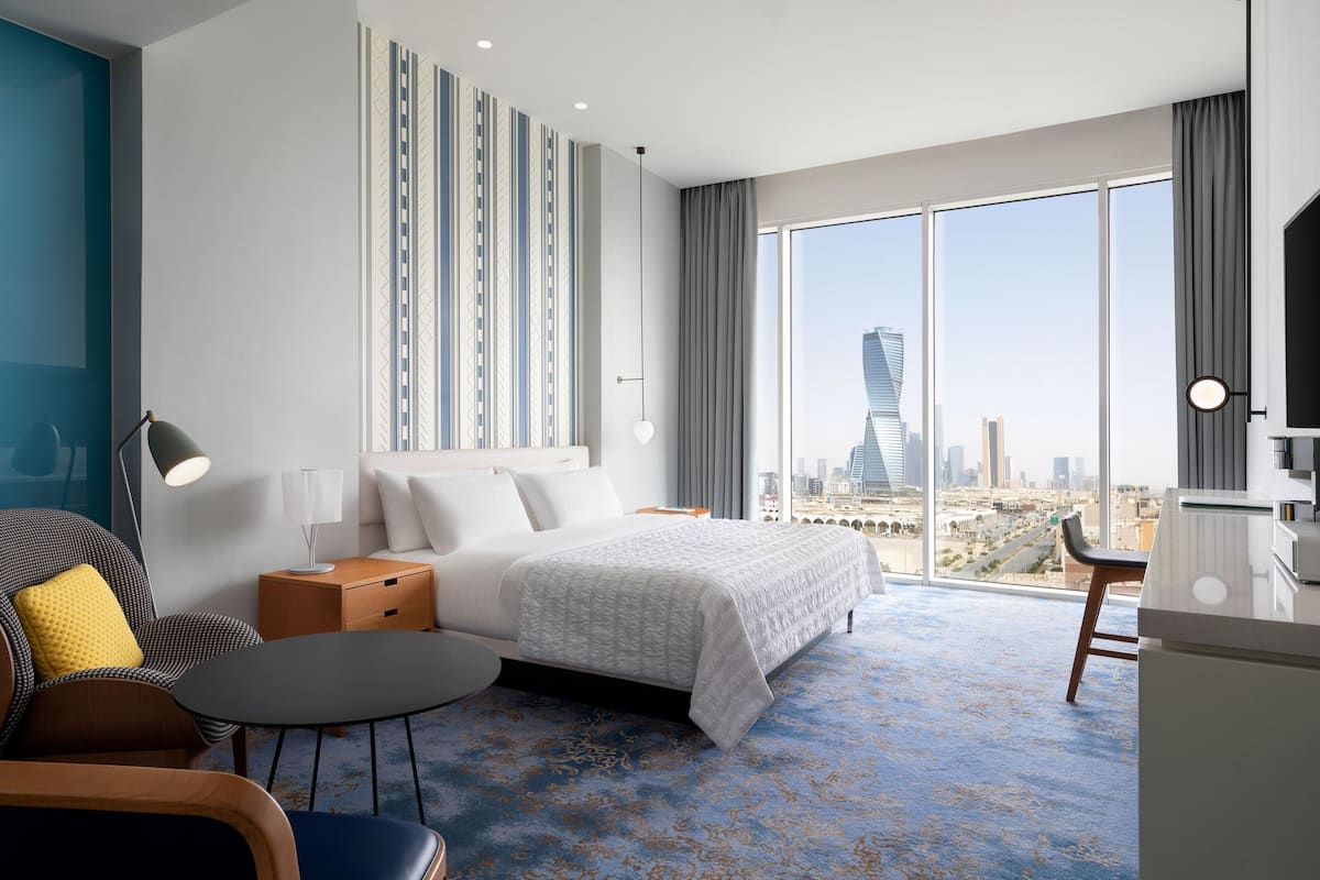 Una habitación de hotel moderna con una cama grande, un escritorio, una silla y vistas a la ciudad.