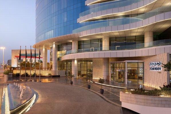 A modern building with a curved facade, large glass windows, and a well-lit entrance area with potted plants and a water feature.