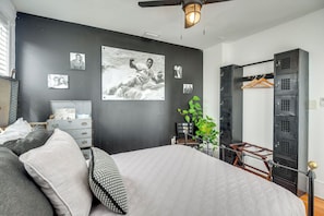 Un dormitorio con cama, cómoda, escritorio, silla, planta y armario.