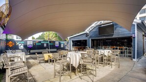 An outdoor patio area with tables and chairs, a covered section, and a building with a bar. - Historic Home < 2 Mi to Daytona Beach & Pier! (Daytona Beach)