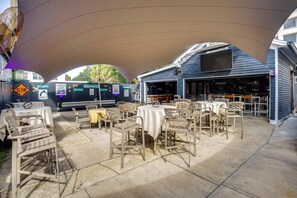Un patio al aire libre con mesas y sillas, una sección cubierta y un edificio con barra.