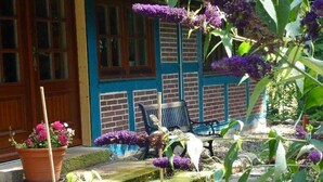 A garden with a brick wall, a wooden door, a bench, and potted plants. - Semi-detached house FeWo 2 - Ferienhäuser Ohlenbusch (Worpswede)
