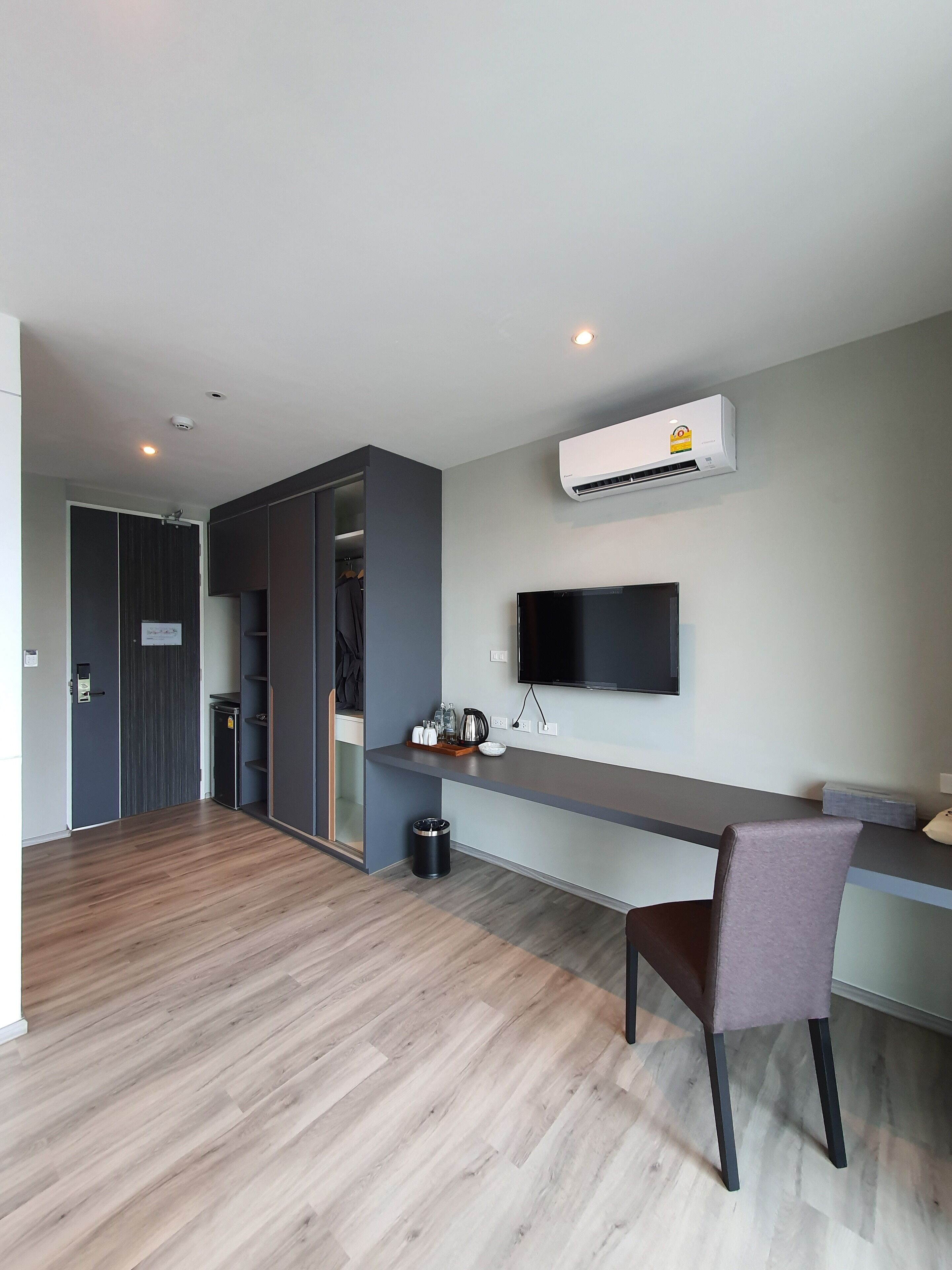 A modern living room with a flat-screen TV mounted on the wall, a built-in air conditioning unit, a wooden floor, and a seating area with a chair and a small table.