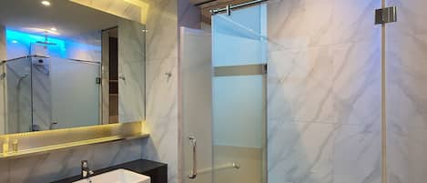 Un baño moderno con ducha de vidrio, tocador con lavamanos y un espejo grande.
