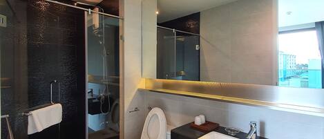 Une salle de bain moderne avec une douche à parois de verre, des toilettes et un lavabo surmonté d’un miroir.