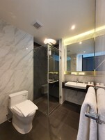 Un baño moderno con ducha de vidrio, inodoro blanco, lavabo con espejo y toallas.