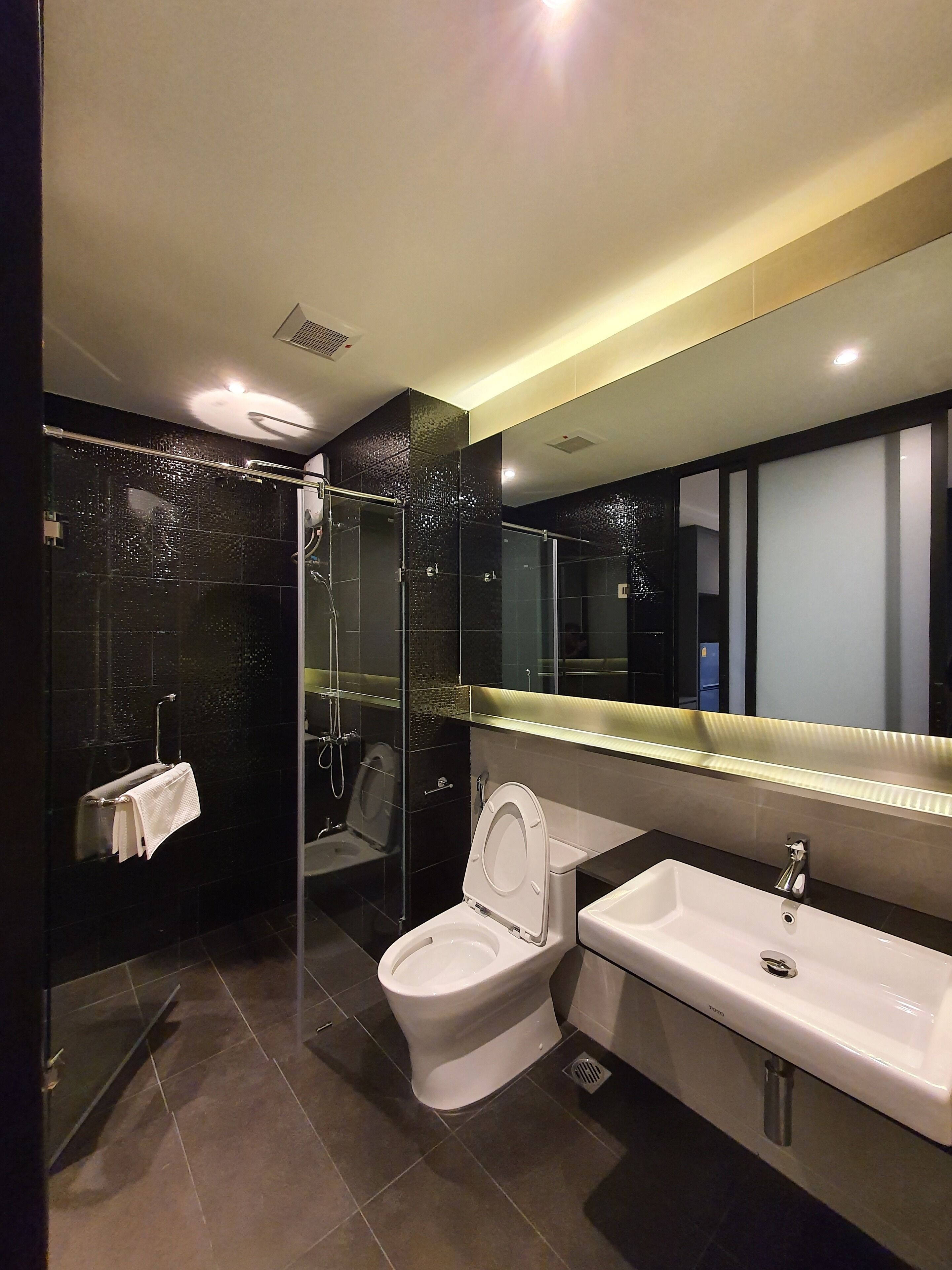 Een moderne badkamer met een douche met glazen wand, een wit toilet en een grote spiegel boven een wastafel.