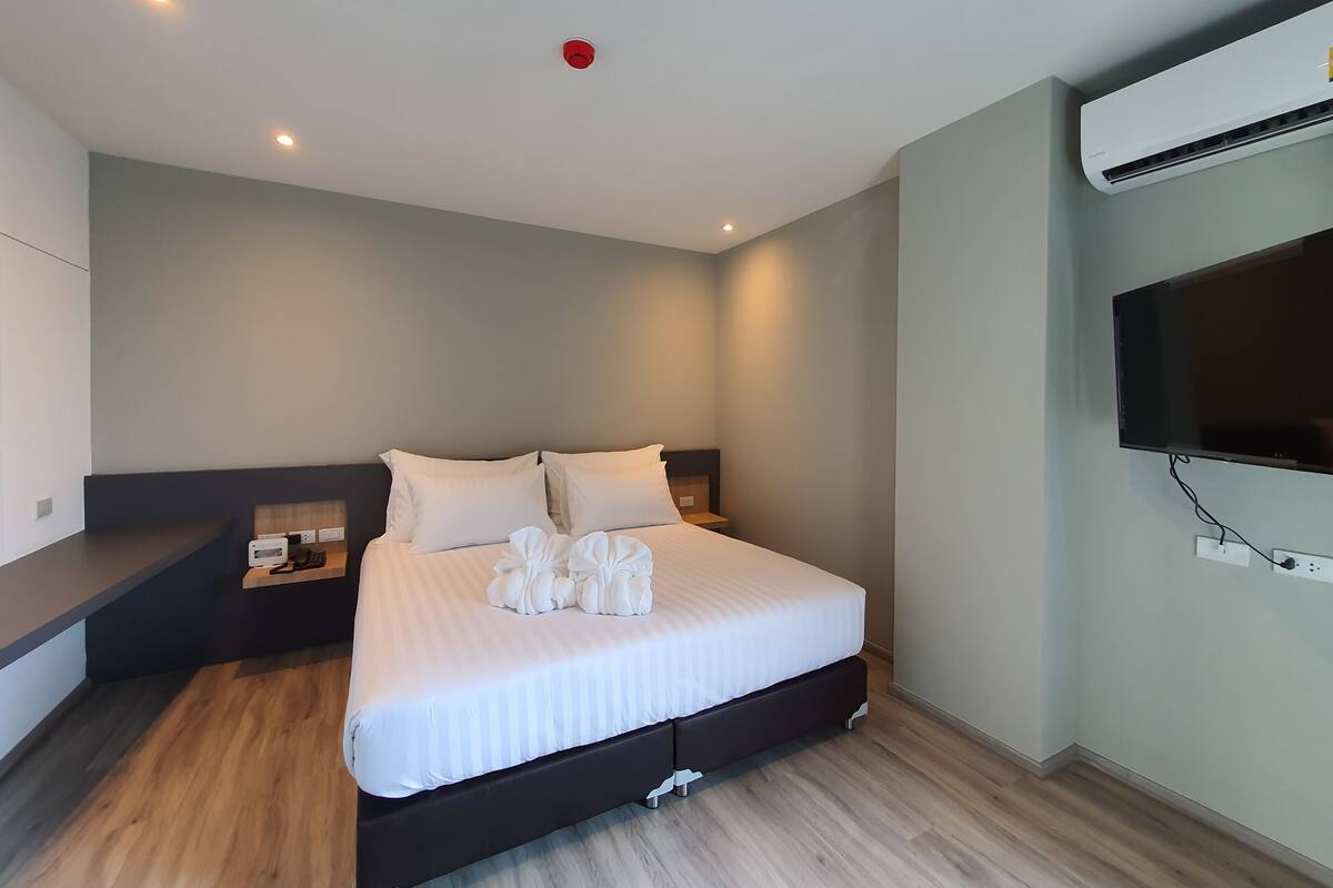 Moderni hotellihuone, jossa on suuri sänky, taulutelevisio ja ilmastointilaite.