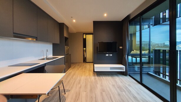 A modern kitchen with a built-in oven, a dining table, and a large window offering a view of the city. - Good Dream Premier (Hat Yai)