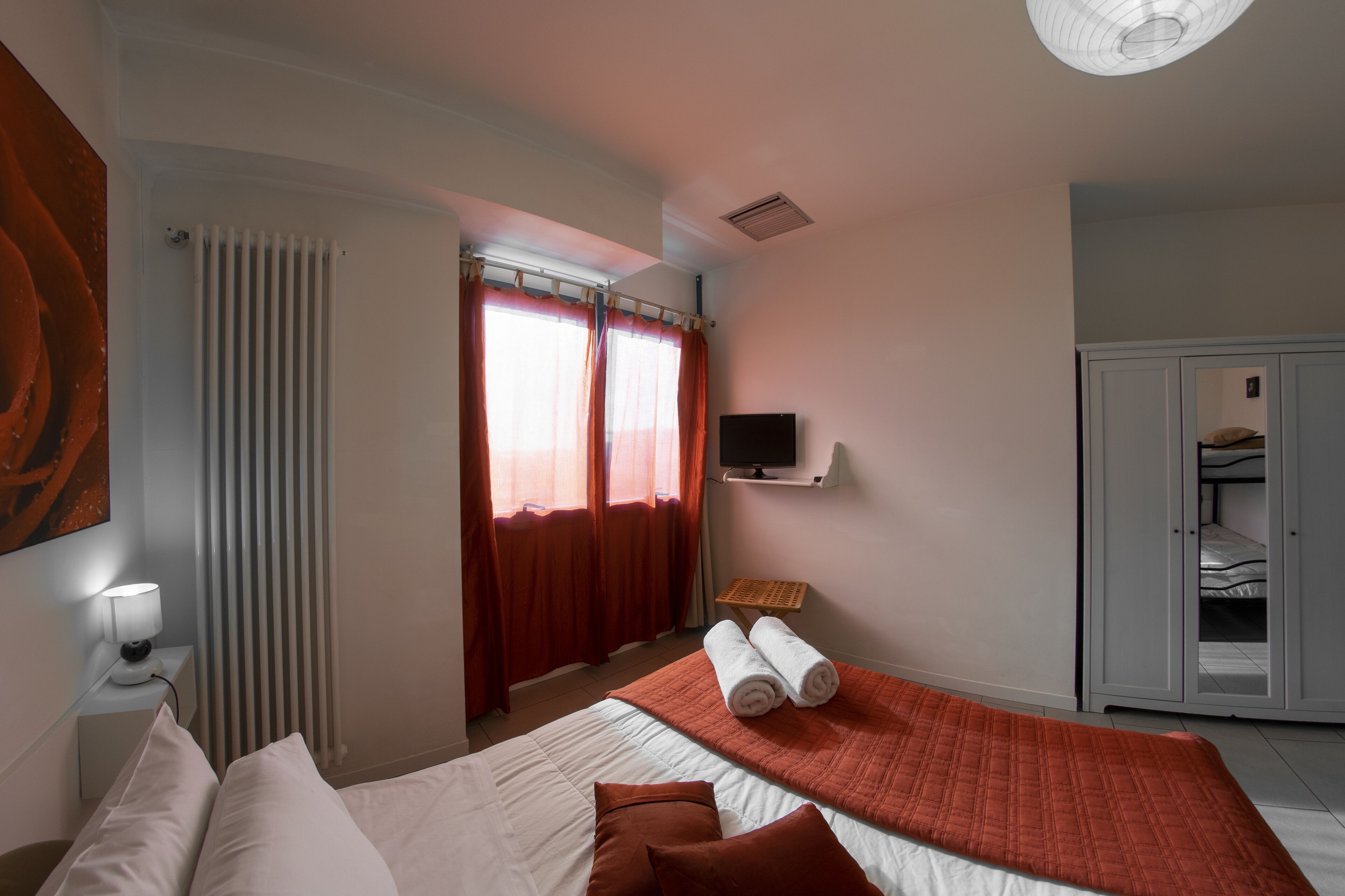 Ein Hotelzimmer mit Bett, Fernseher, Kleiderschrank und einem Fenster mit Vorhängen.