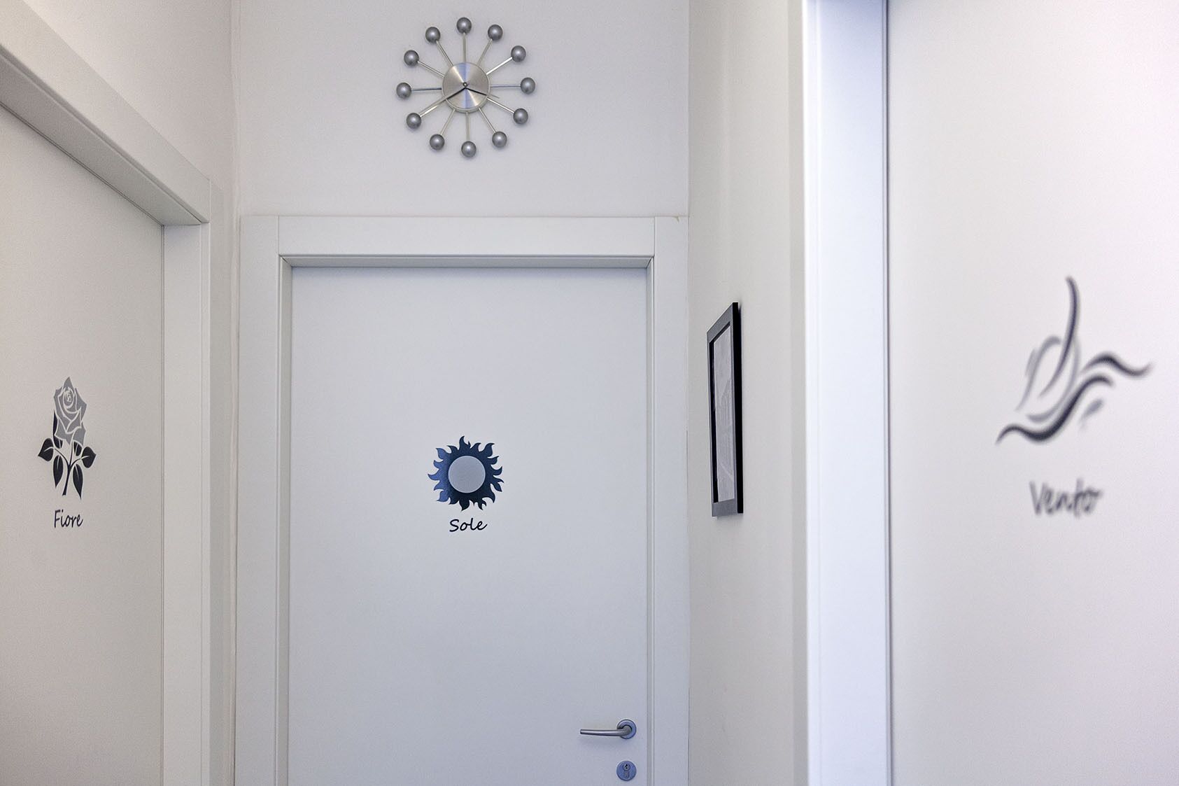 A hallway with a white door, a clock, and wall art including a rose, sun, and a logo.