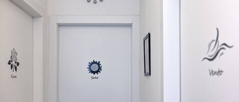A hallway with a white door, a clock, and wall art including a rose, sun, and a logo.