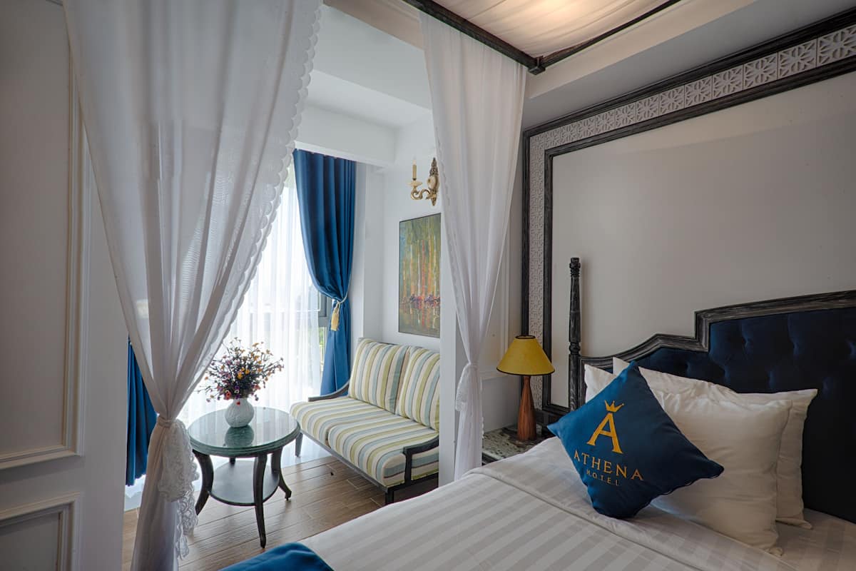 Quarto de hotel com cama, sofá, uma pequena mesa com um vaso e uma luminária.