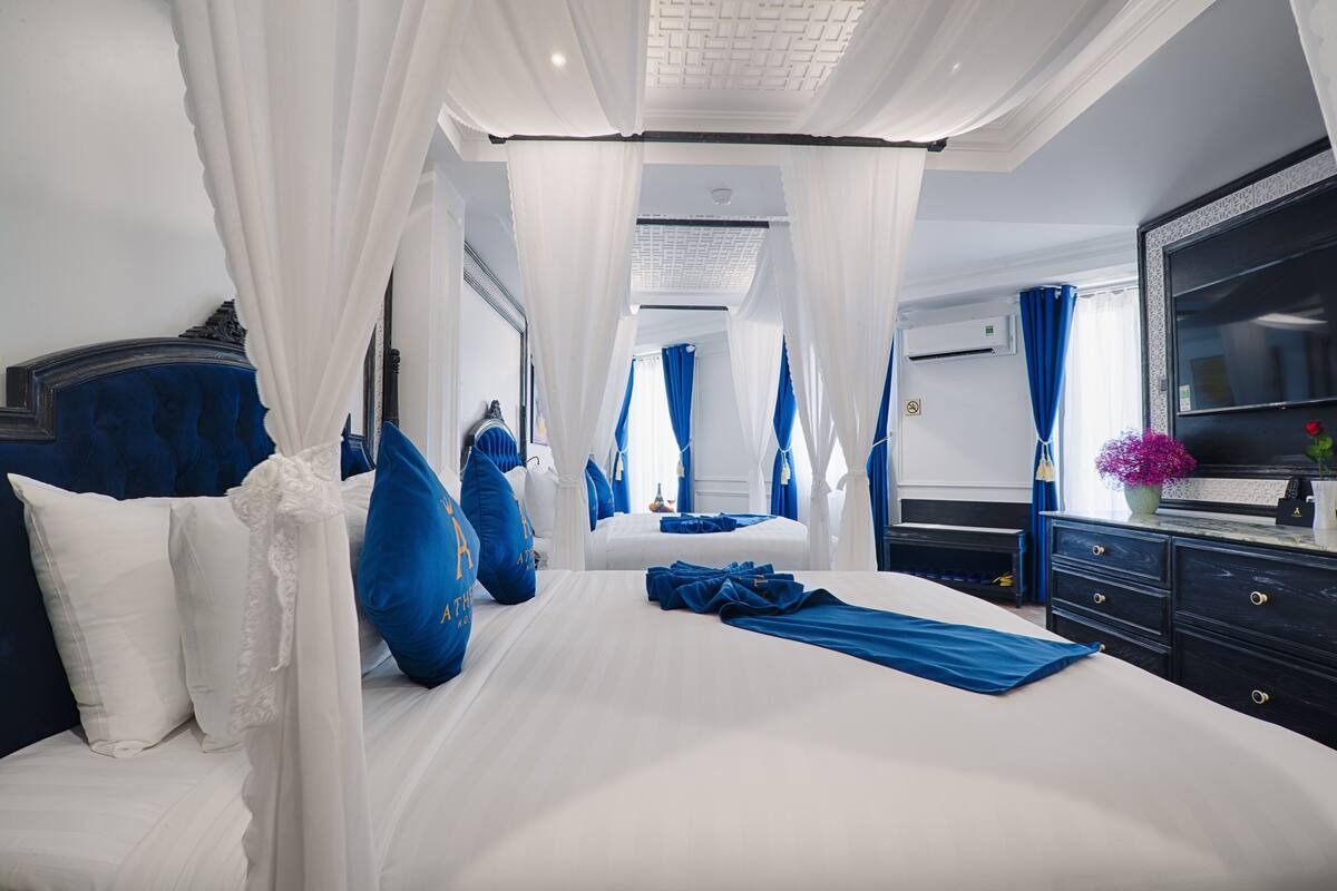 Quarto com uma cama grande, roupa de cama branca e azul, um dossel e uma cômoda com espelho.