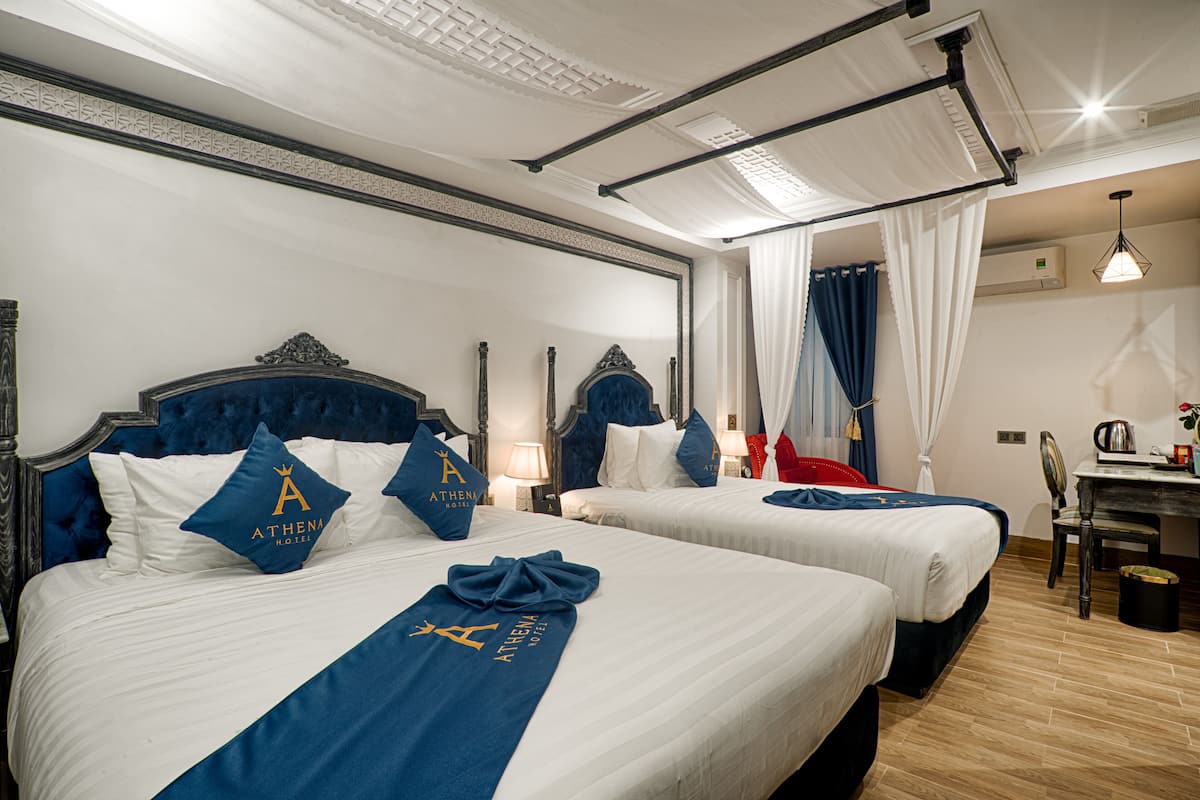 Quarto de hotel com duas camas, cada uma com cabeceira, uma escrivaninha e uma cadeira.