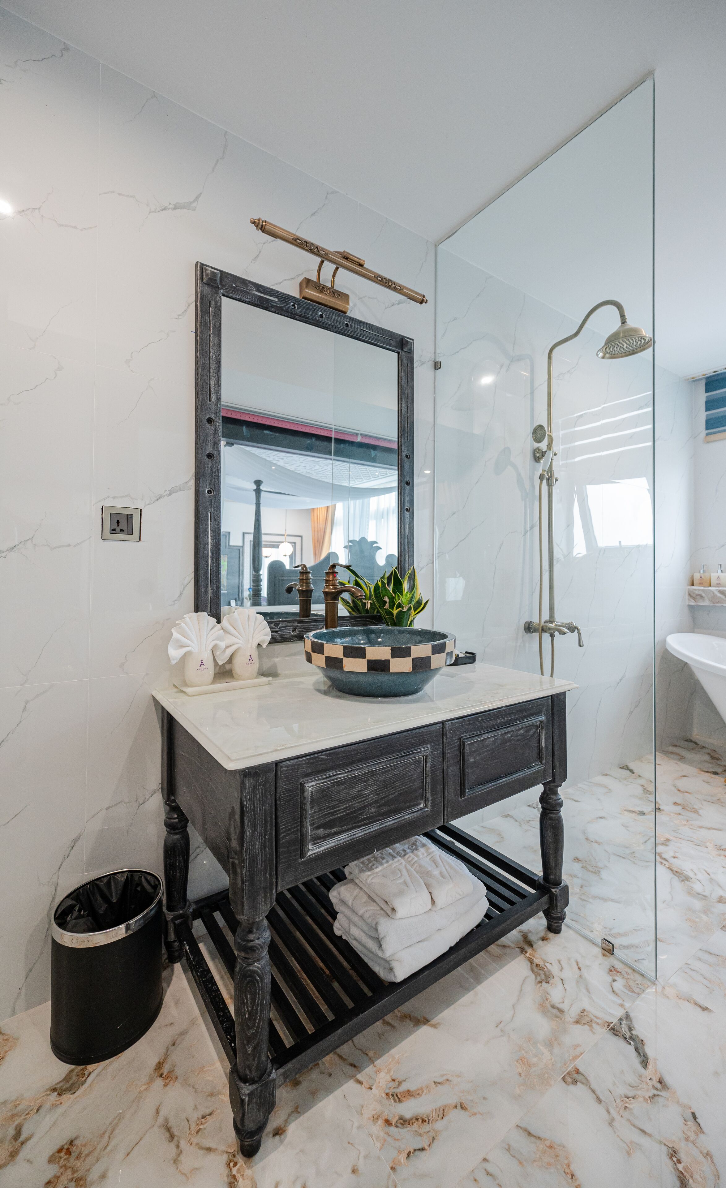 A bathroom with a marble floor, a round sink with a checkered bowl, a dark wooden vanity, a large mirror, and a glass shower enclosure.