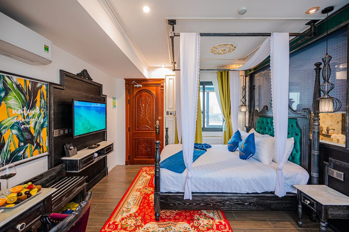 Quarto de hotel com cama, televisão, obras de arte e tapete vermelho.