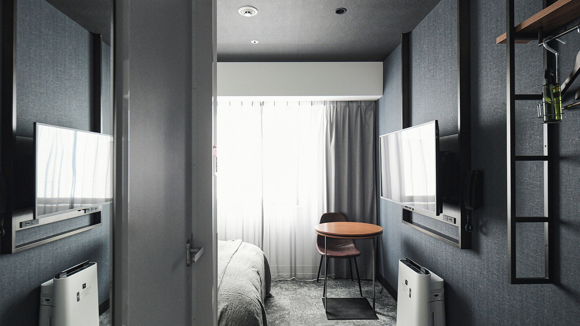 Una habitación de hotel moderna con una cama, un escritorio, dos televisores, una silla y una pequeña mesa.
