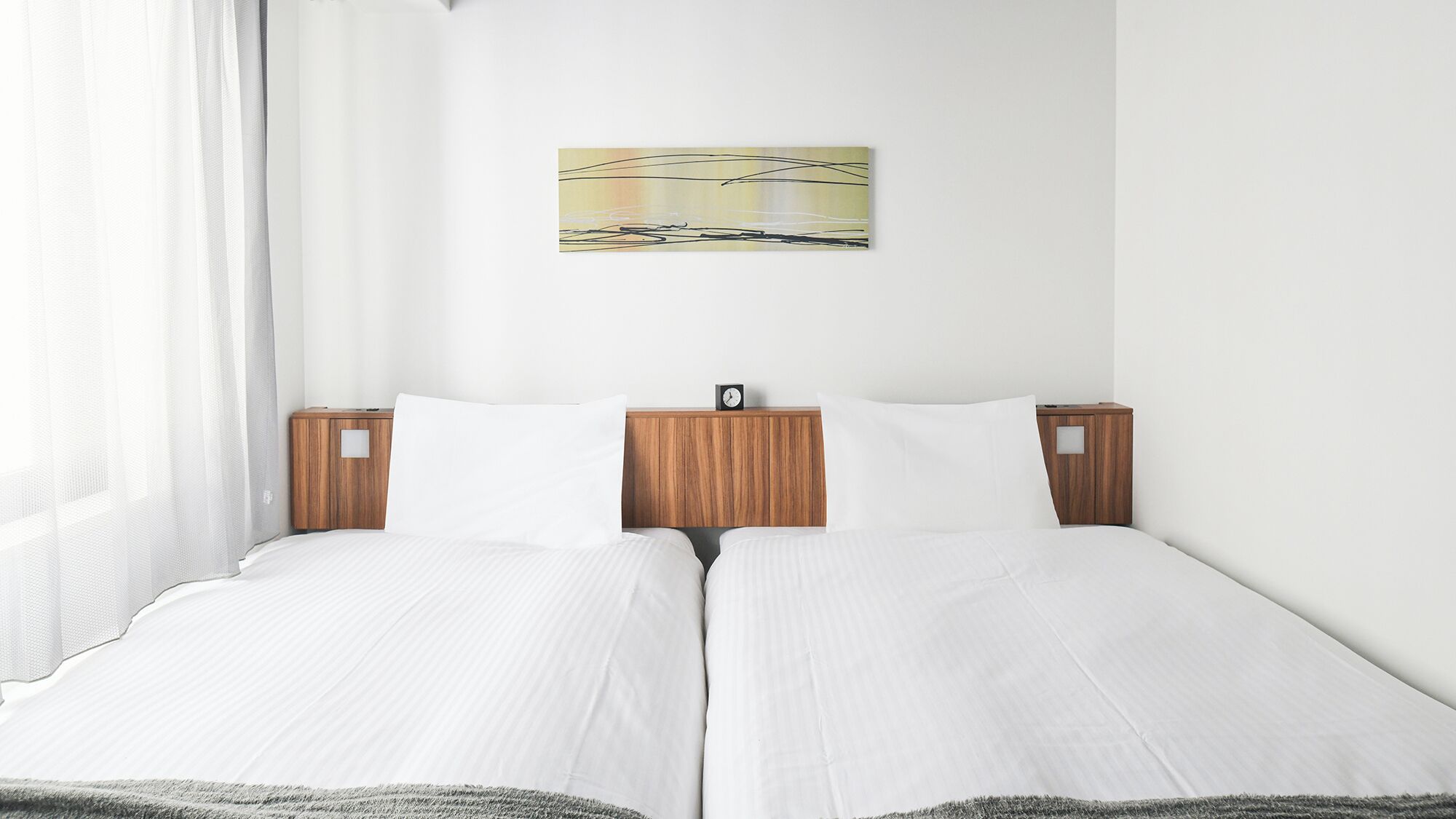 Una cama doble con cabecera de madera, ropa de cama blanca, un pequeño reloj y un cuadro en la pared.