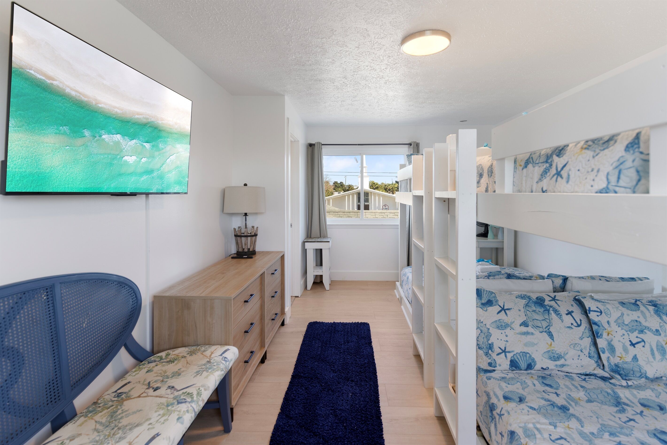 Un couloir étroit avec un tapis bleu, un banc, une commode en bois et un lit superposé sur le thème de la marine.