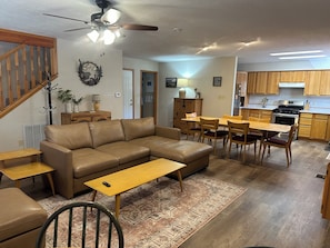 A living room with a sofa, a dining table, and chairs, a kitchen with wooden cabinets, and a ceiling fan. - KXDJ Riverside 1 on the River (Red River)