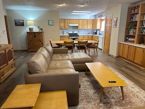A living room with a sofa, coffee table, and chairs, a kitchen with wooden cabinets, and a dining area with a table and chairs. - KXDJ Riverside 1 on the River (Red River)